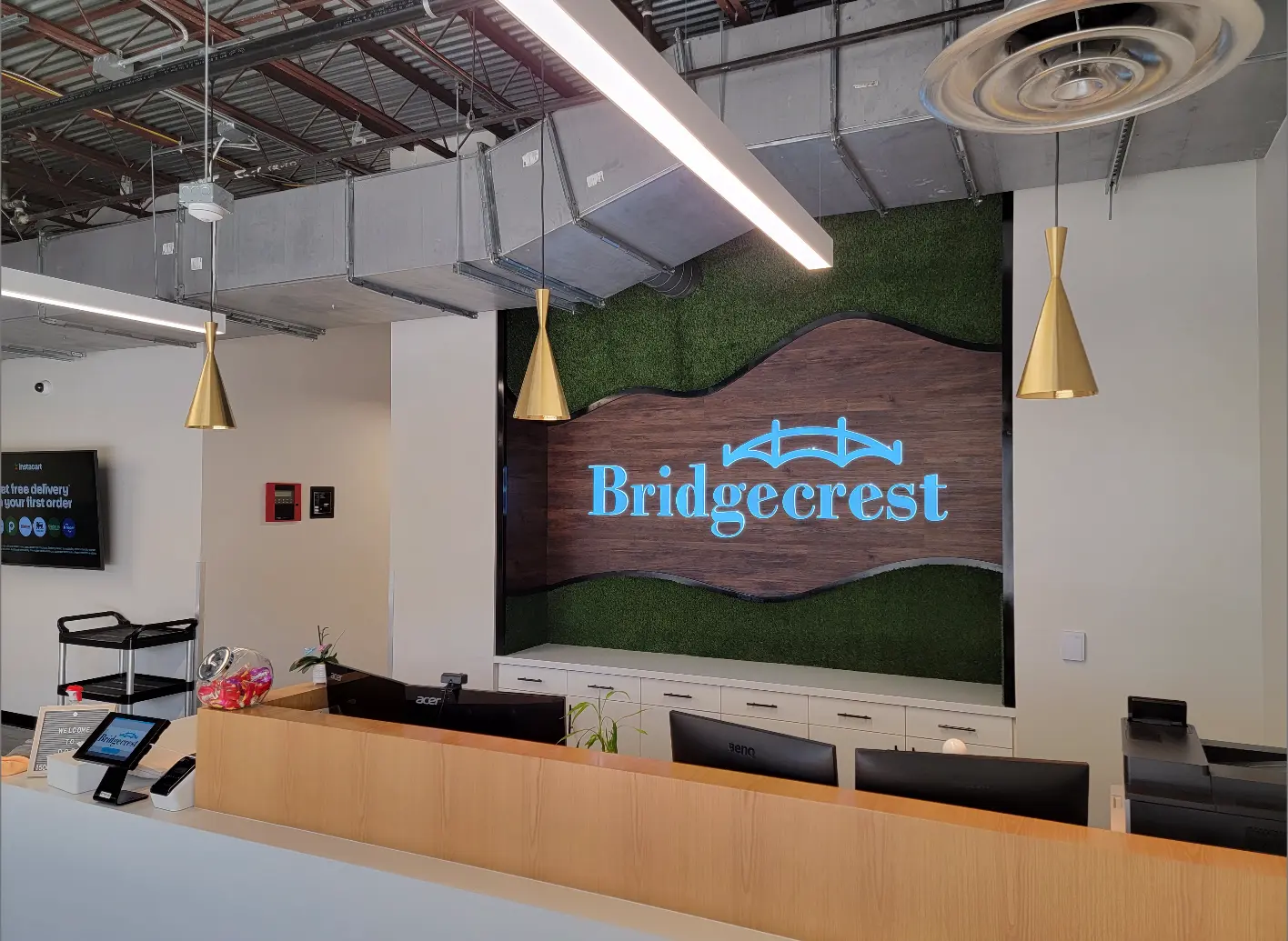 Bridgecrest branded reception area design with illuminated dimensional logo wall, layered wood and living greenery feature wall, and permanent interior installation by Highway 85 Productions