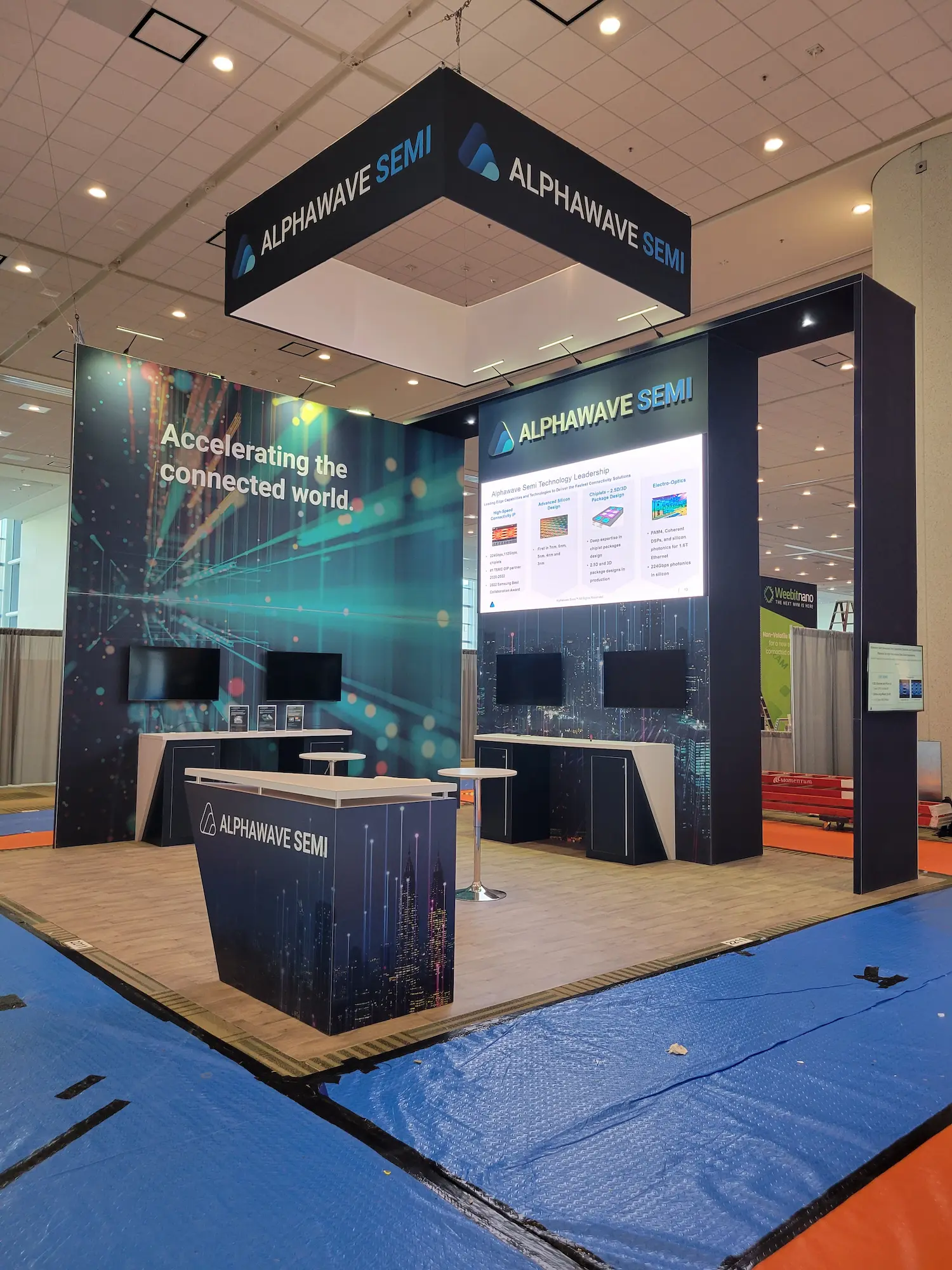 Alphawave Semi 20x20 large custom trade show booth with hanging sign, backlit graphics, branded counters, and LED display wall by Highway 85 Productions