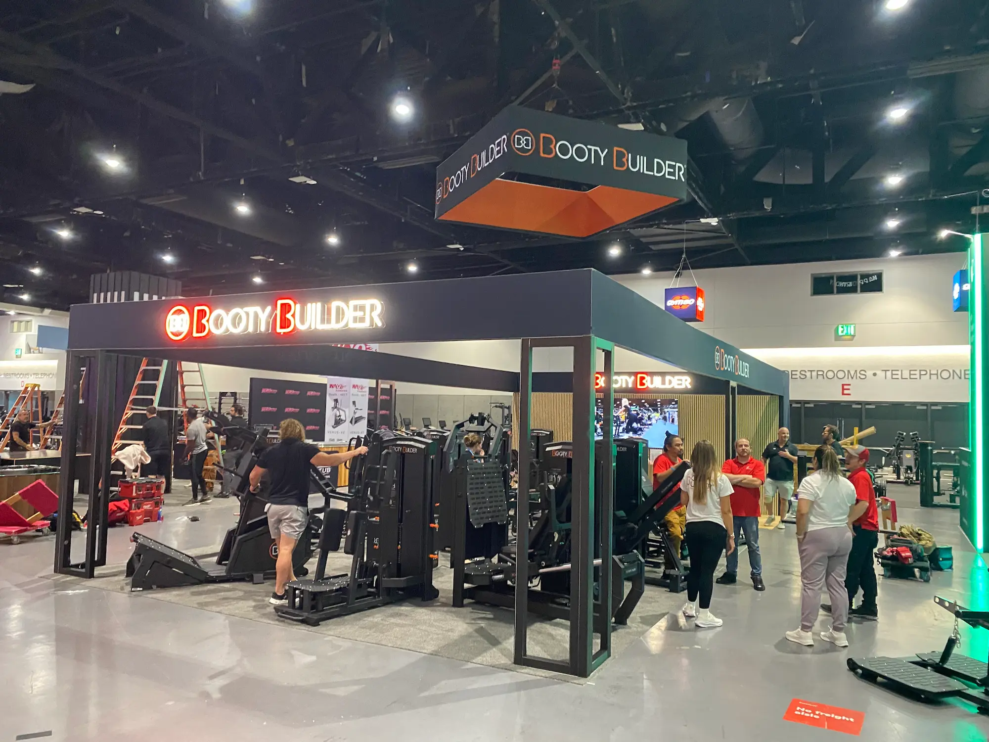 Booty Builder 20x40 custom trade show booth installation in progress on the show floor with crew assembling branded structure and hanging sign by Highway 85 Productions
