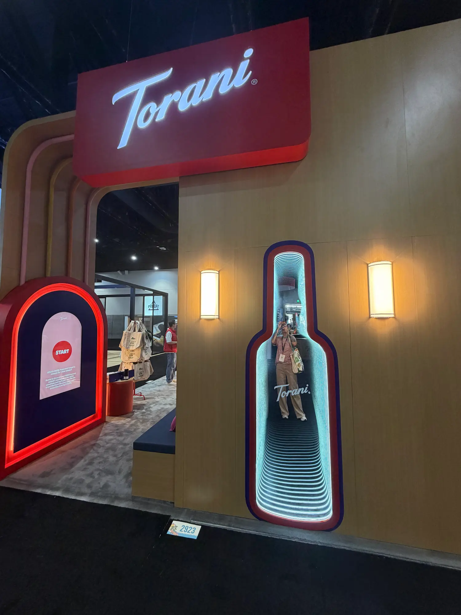 Torani custom trade show booth with interactive infinity mirror bottle display, branded LED lighting, and touchscreen kiosk showing trade show booth technology integration by Highway 85 Productions