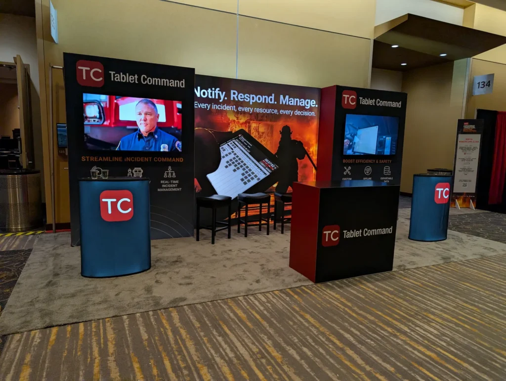 10×20 Tablet Command trade show booth with a concise headline, repeated branding, video displays, and high-contrast red and black graphics.